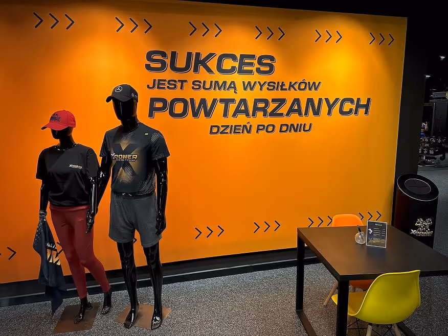 Dwa manekiny prezentujące ubrania XPower, a w tle grafika na ścianie z motywującym hasłem.