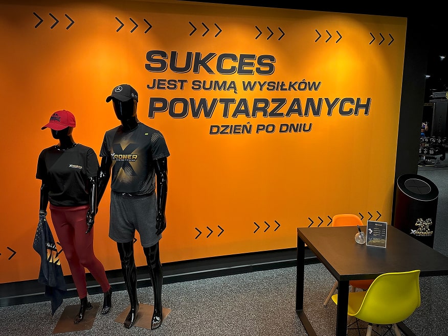Dwa manekiny prezentujące ubrania XPower, a w tle grafika na ścianie z motywującym hasłem.