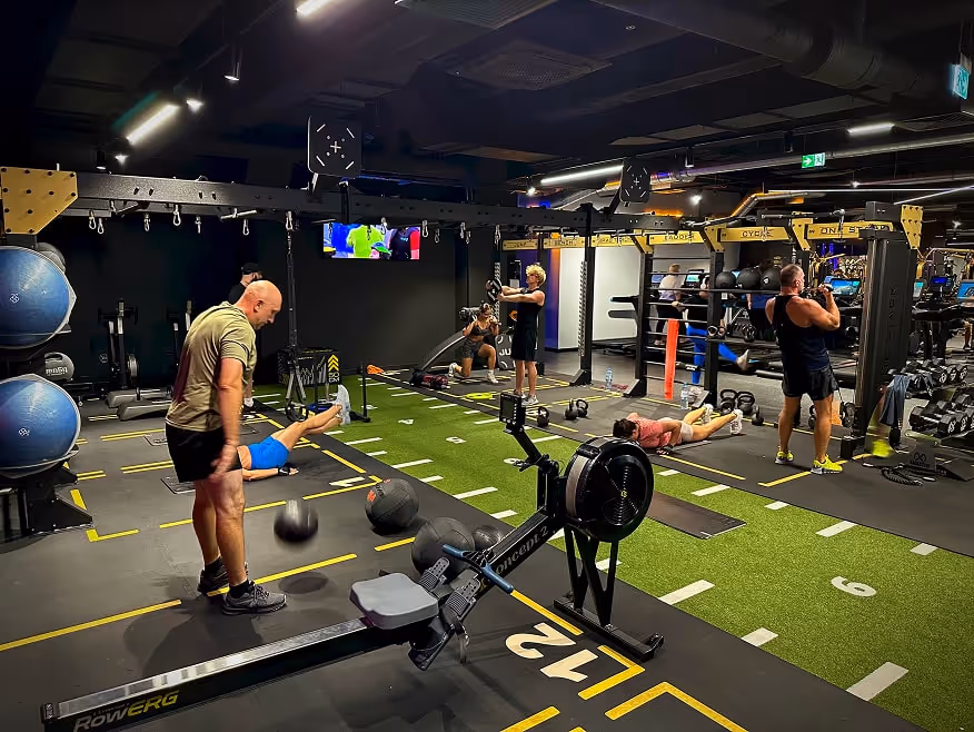 Strefa funkcjonalna z grupowymi zajęciami fitness, wykorzystująca różnorodny sprzęt i podział na stacje ćwiczeń.