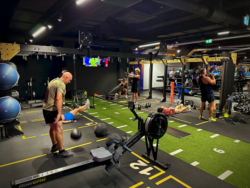 Strefa funkcjonalna z grupowymi zajęciami fitness, wykorzystująca różnorodny sprzęt i podział na stacje ćwiczeń.