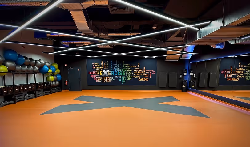 Widok na salę do zajęć fitness. Przestronne wnętrze z dużymi lustrami, sprzętem do ćwiczeń grupowych i nowoczesnym wyglądem.