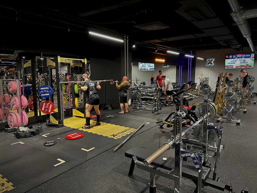 Mężczyzna wykonujący przysiady ze sztangą w strefie wolnych ciężarów na siłowni.